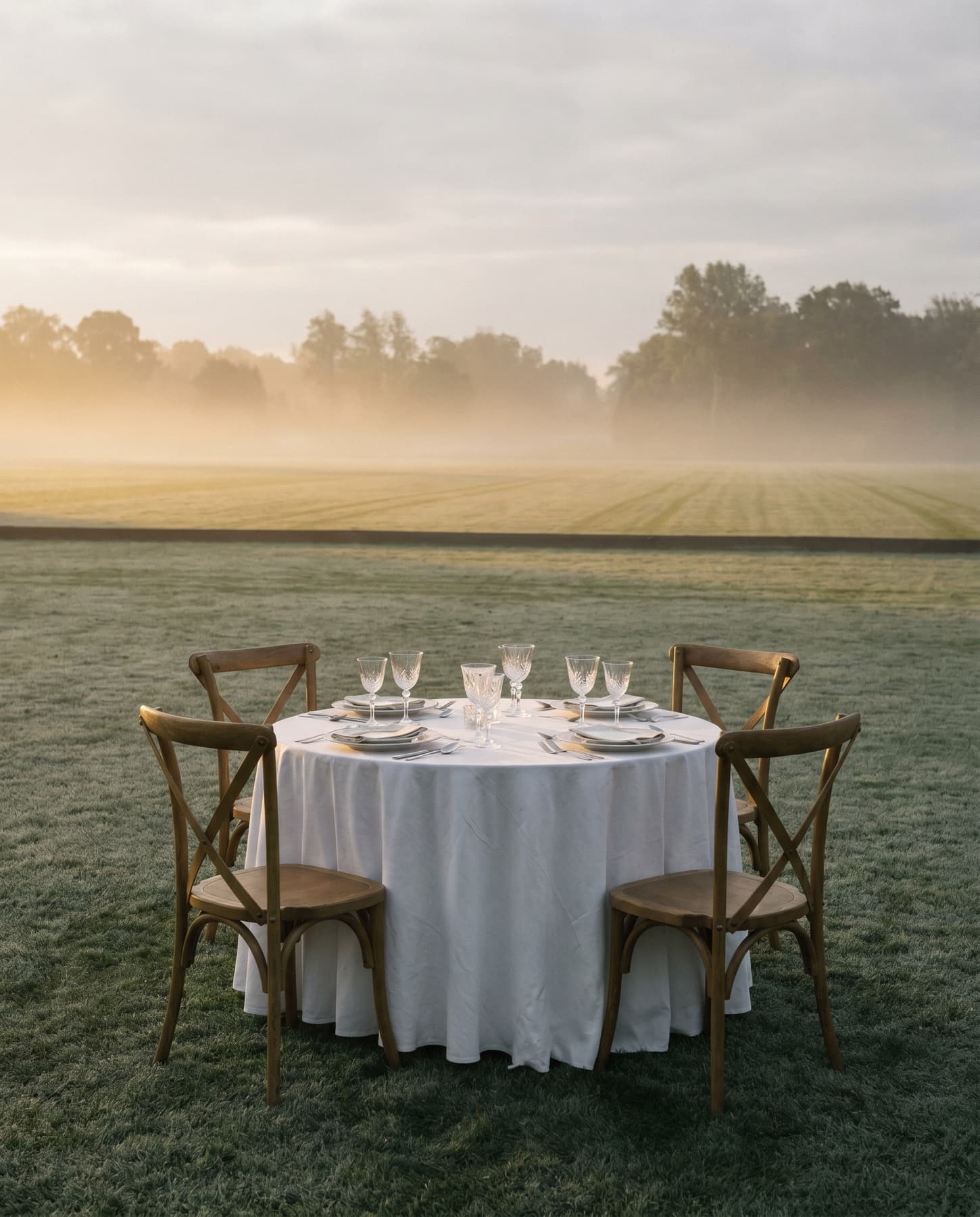 A white-clothed table set and waiting on the polo lawn at dawn.